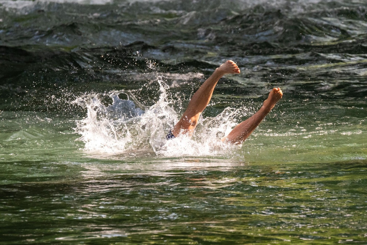 Ein junger Mann erfrischt sich mit einem Sprung in den Eisbach im Englischen Garten in München.