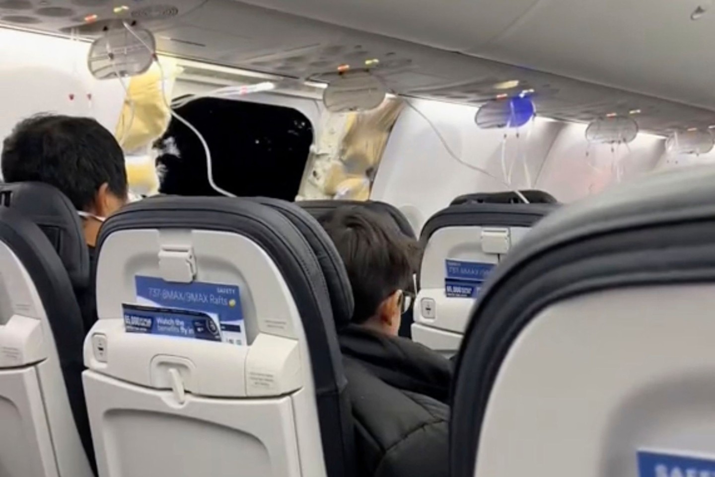 Passagiere sitzen in einer Boeing 737-9 Max in der Nähe des abgerissenen Kabinenteils.