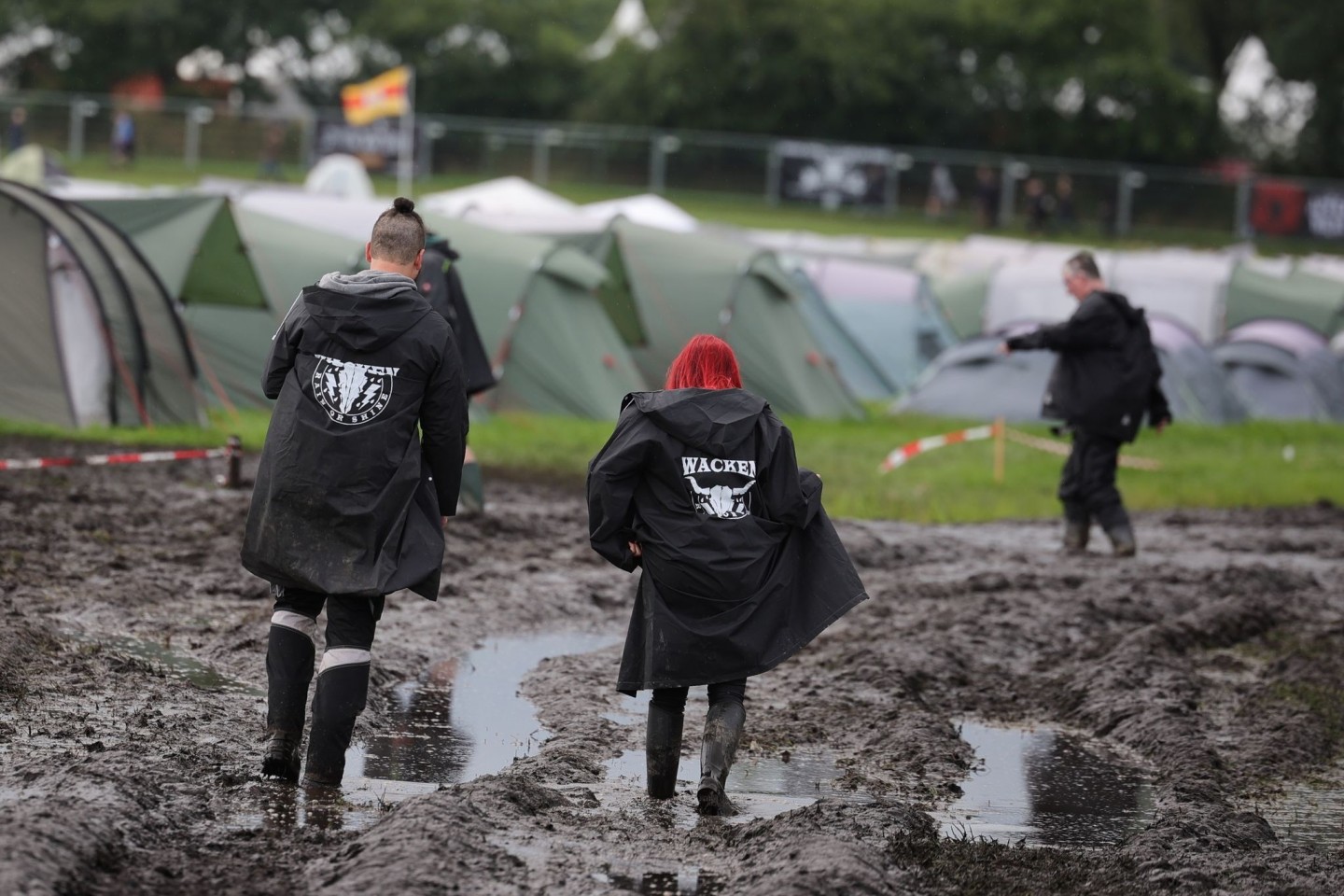 Metal-Fans sind auf dem schlammigen Festivalgelände unterwegs.