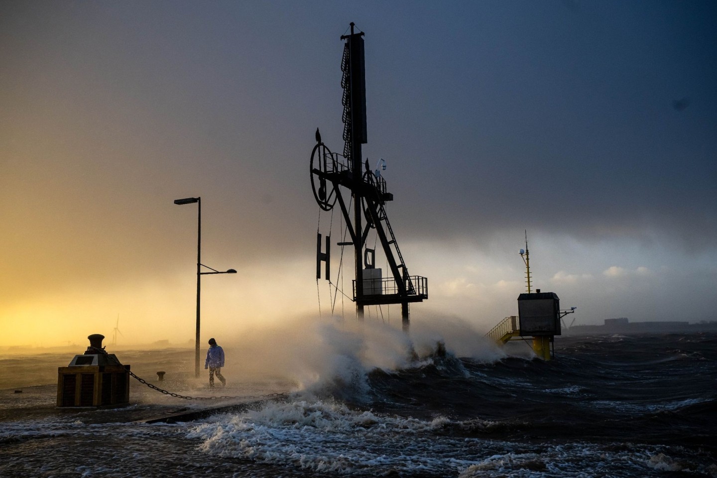 Ein Spaziergänger läuft bei Sturmflut und Wellen am Ufer der Wesermündung in Bremerhaven entlang.