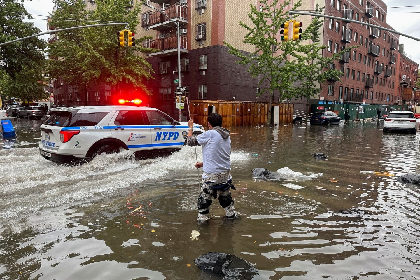 Hochwasser auf den Straßen von New York: Im Stadtteil Brooklyn versucht ein Mann, mit einem Stock einen Abfluss zu reinigen, während ein Polizeiwagen vorbeifährt.