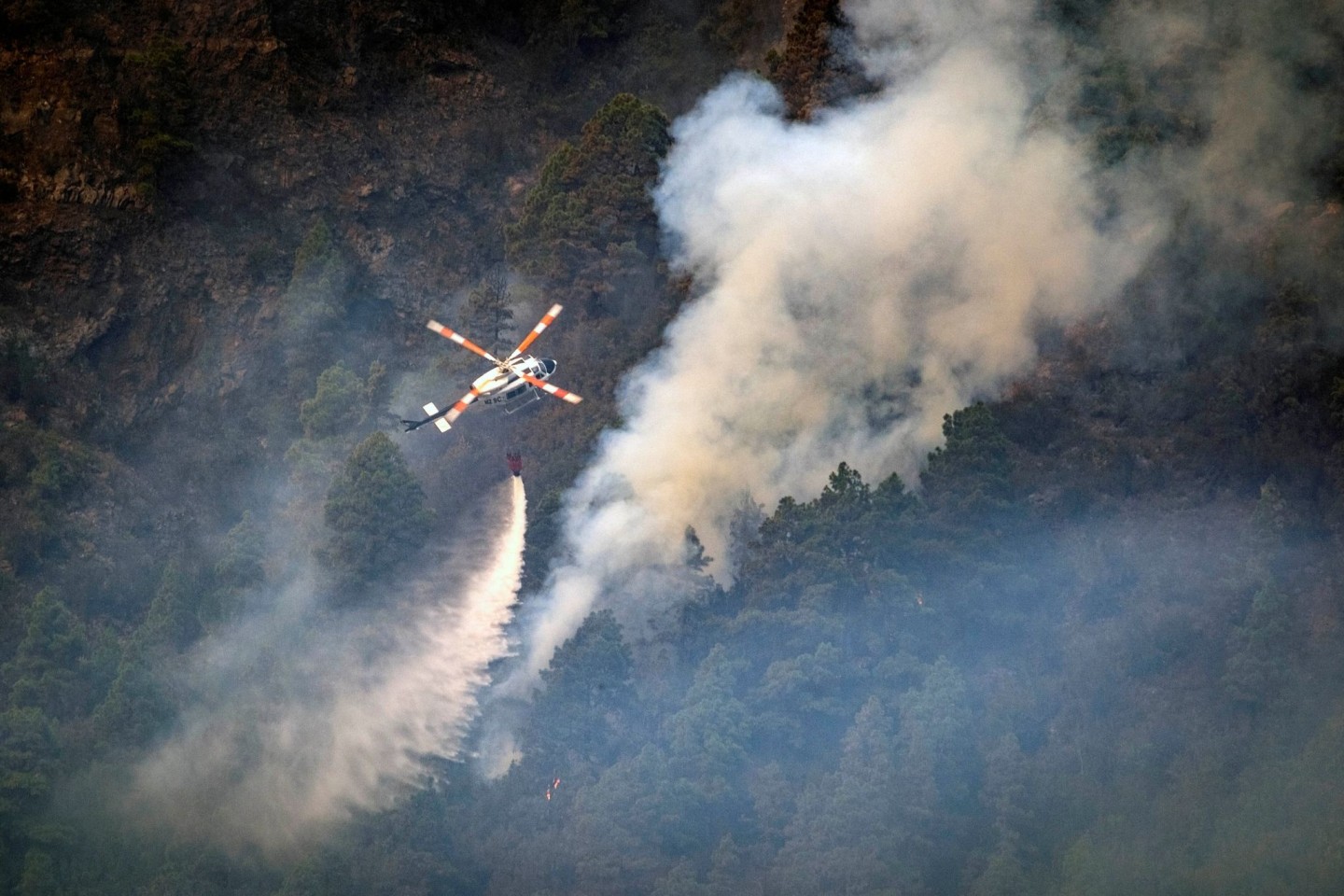 Ein Hubschrauber wirft Wasser auf die Flammen, während sich das Feuer durch den Wald in Richtung der Stadt Pinolere ausbreitet.